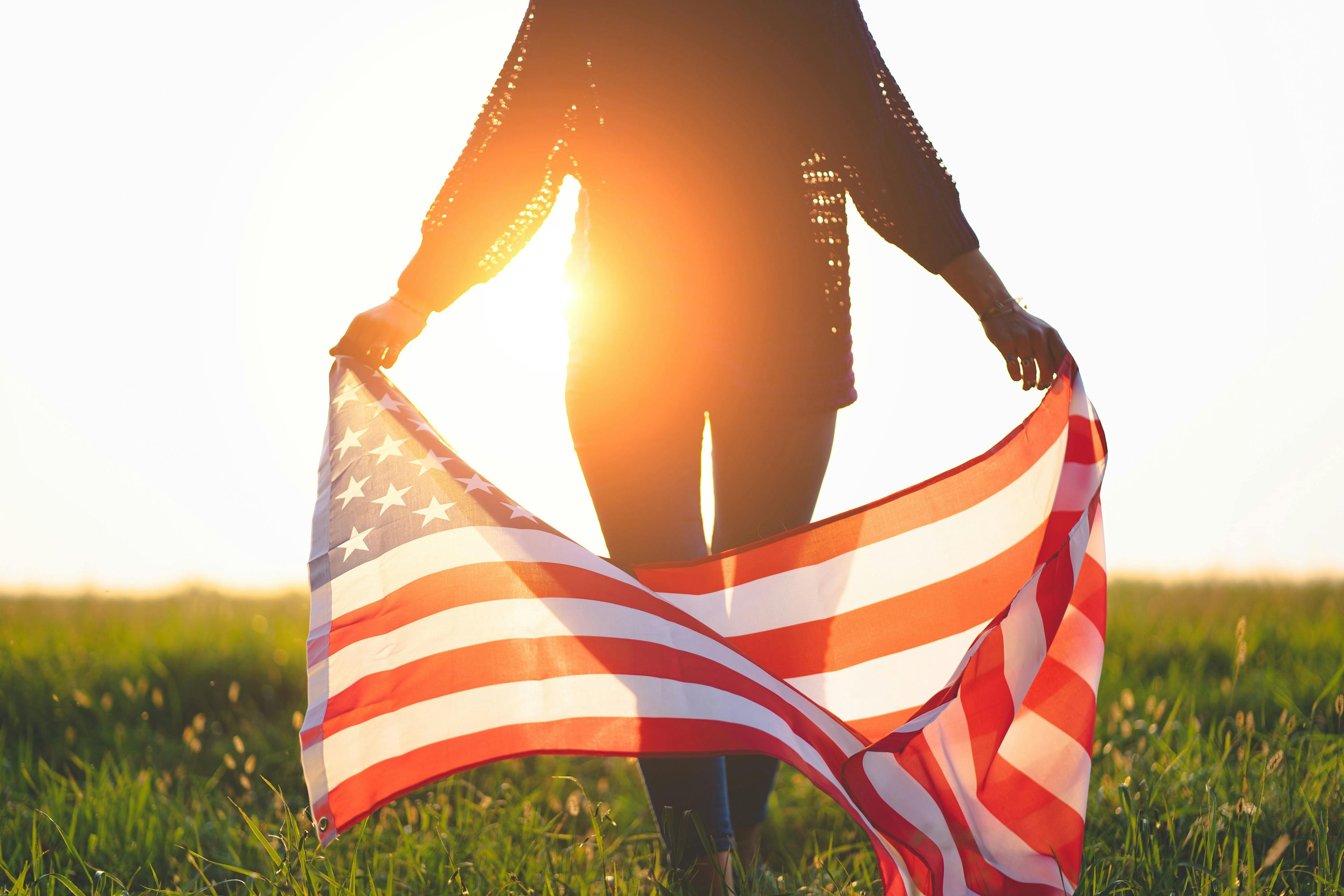 person holding American flag at sunset