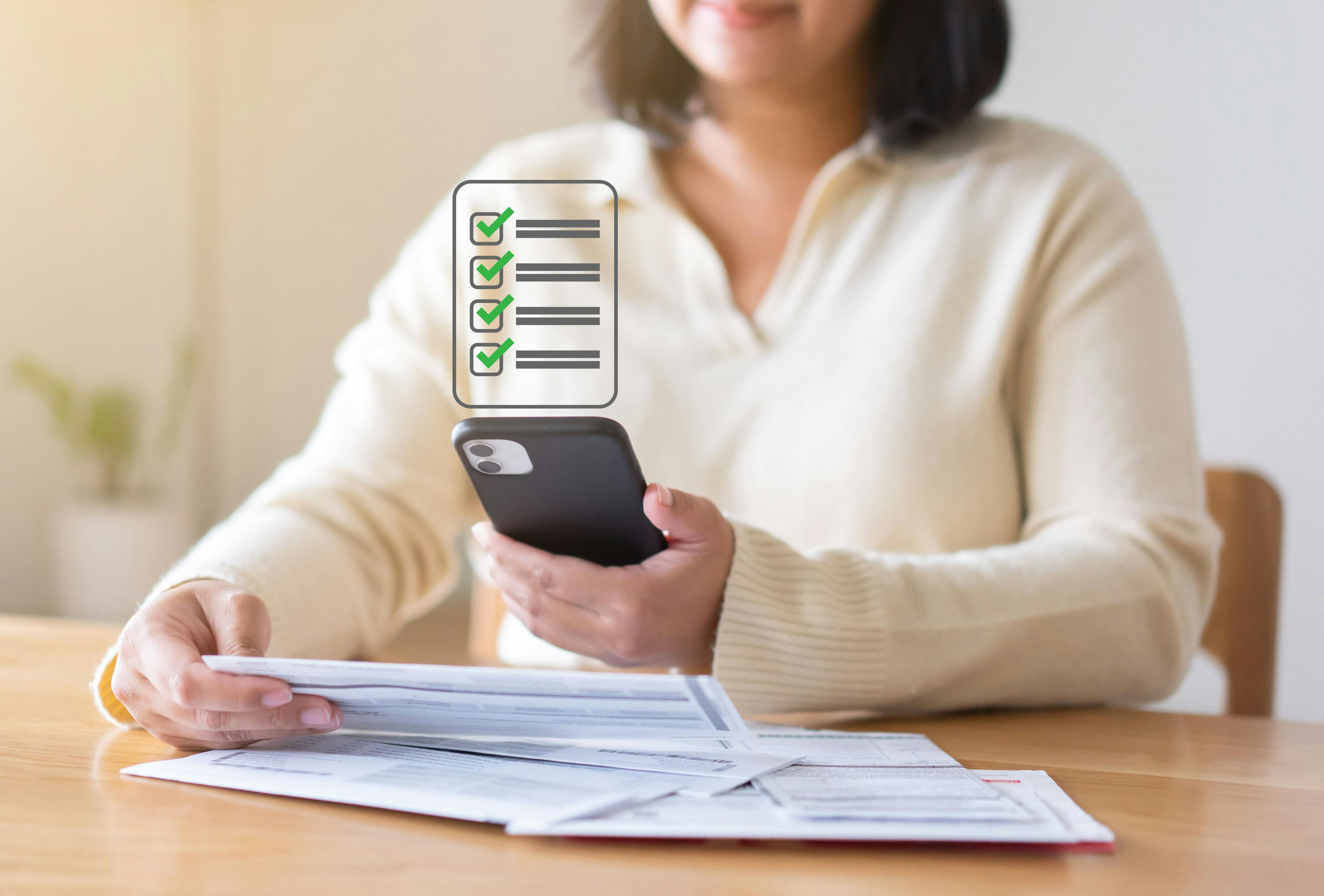 Woman looking at cell phone with stack of documents ©StockerThings -stock.adobe.com