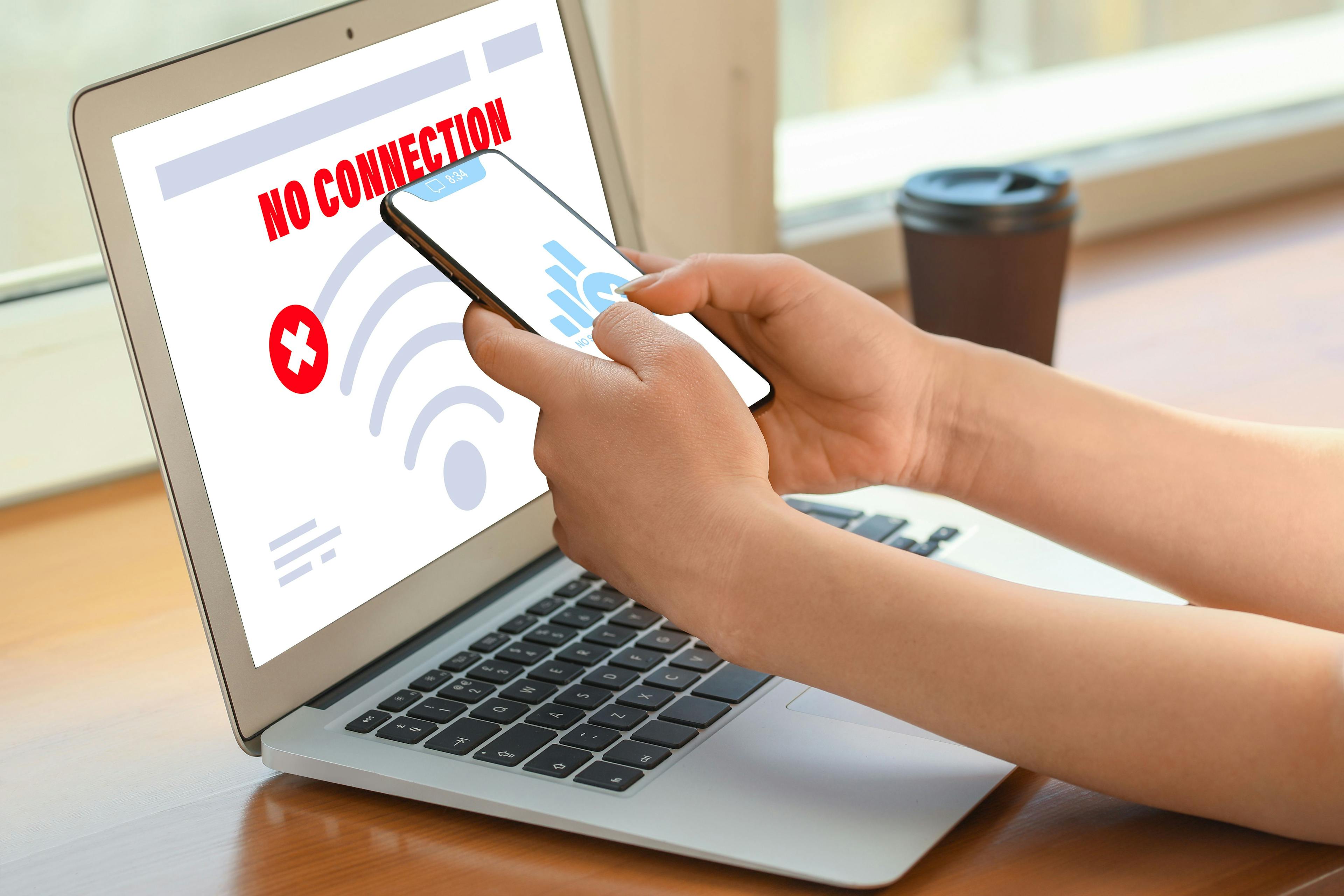 "No connection" displayed on laptop with person holding cellphone ©Pixel-Shot-stock.adobe.com