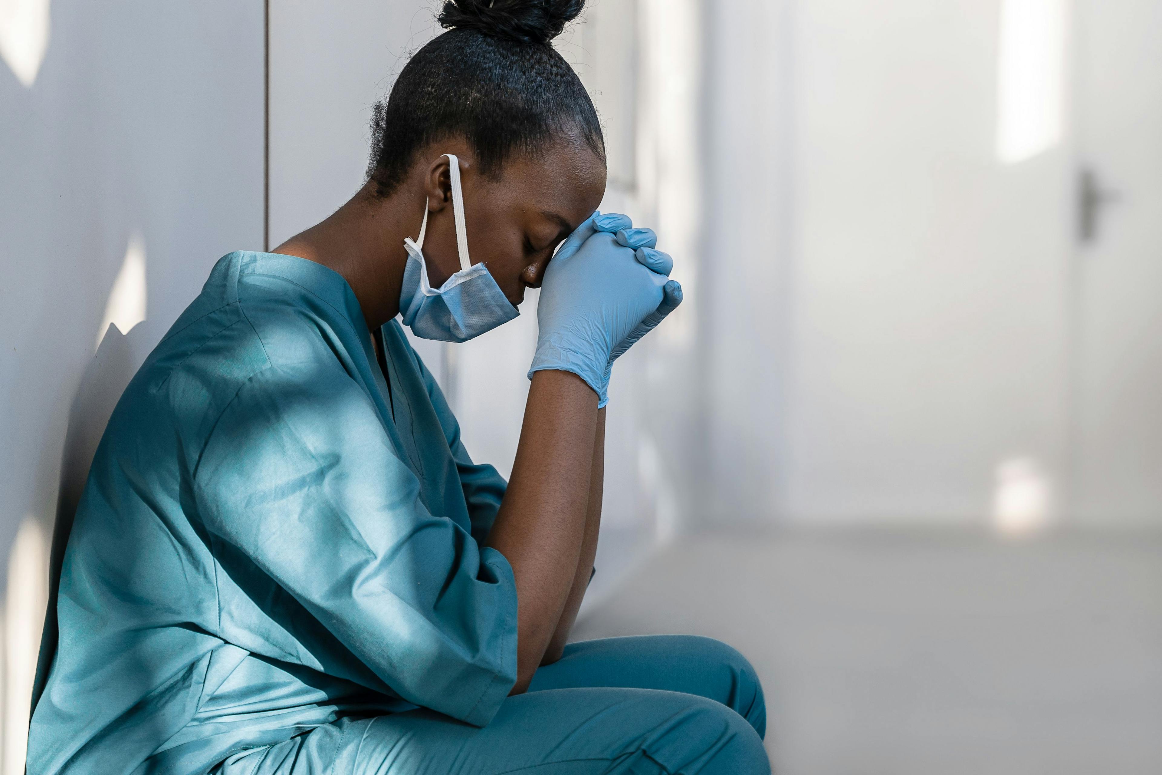 Black nurse in scrubs with hands clenched on forehead ©insta_photos-stock.adobe.com